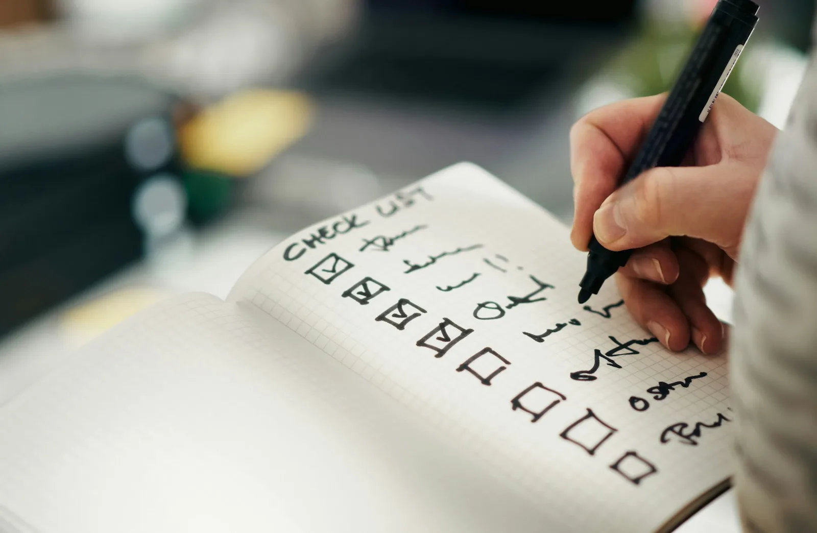 A hand with a marker ticking boxes down a handwritten checklist in a notebook.